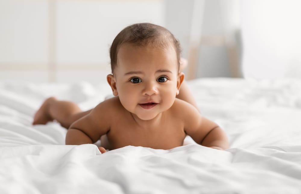 Bébé nu et souriant, allongé sur le ventre dans un lit